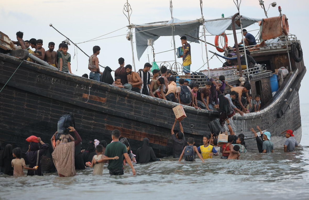 Rohingya refugees disembark from a crowded boat into shallow water
