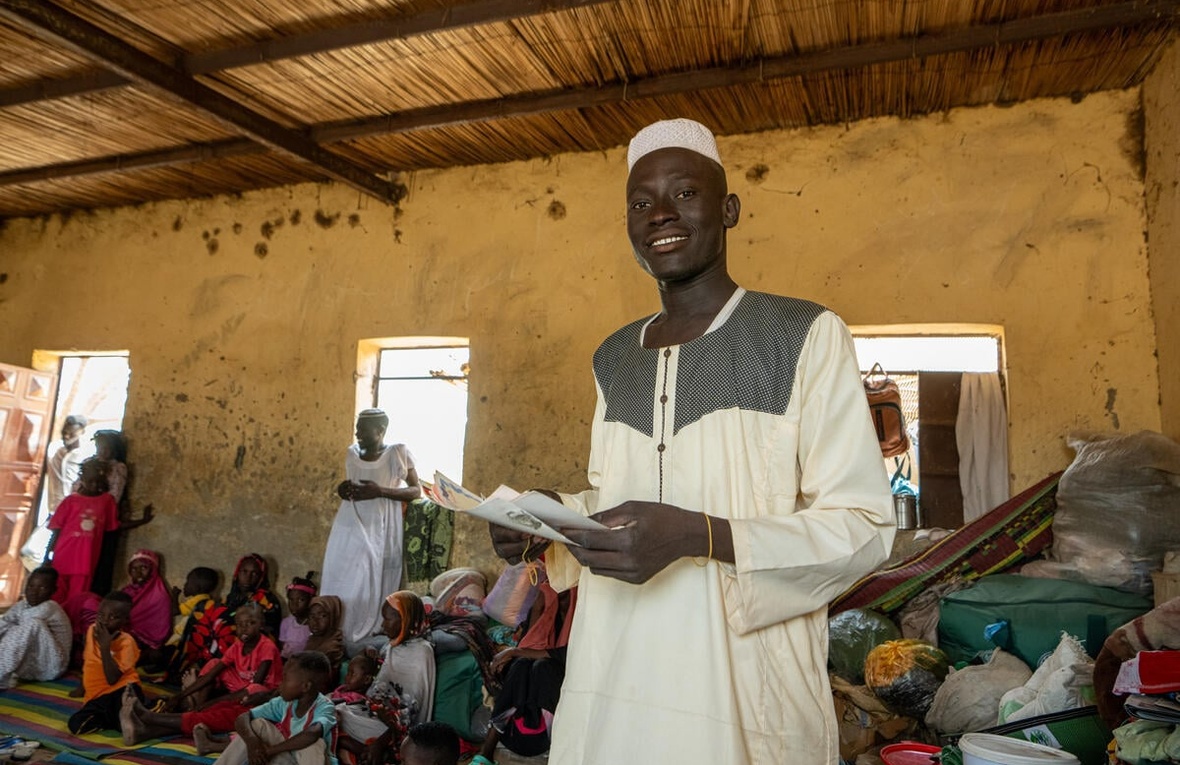 A young man holds some documents in a crowded room.