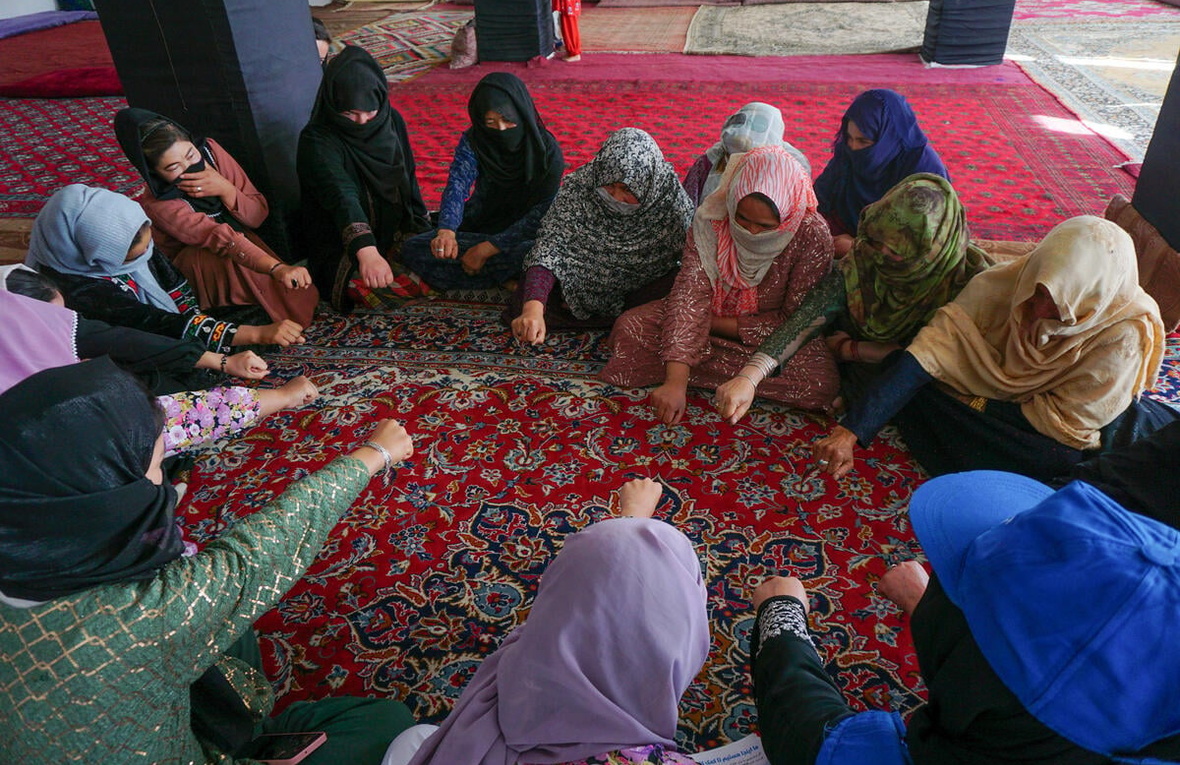 A group of women seated in a circle on a rug put their fists together.