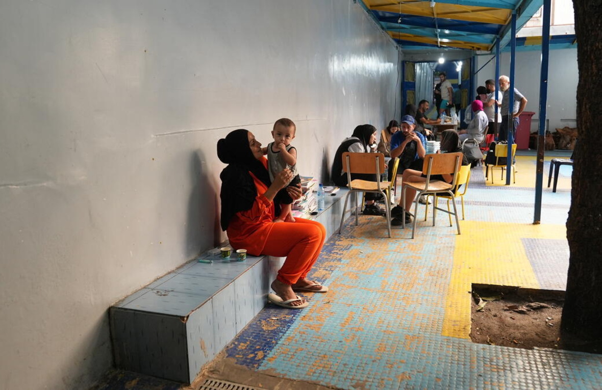 A woman sits on a ledge in a courtyard with a small boy standing on her lap.