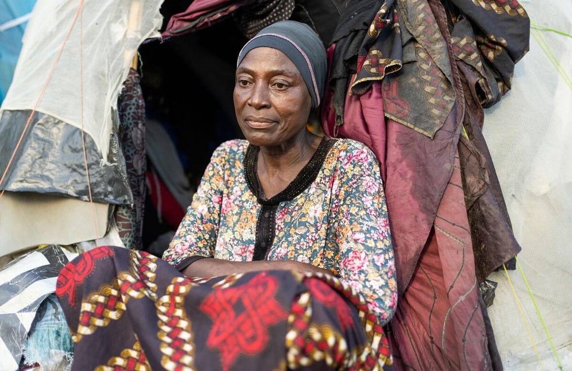 A woman sits in front of a makeshift shelter.