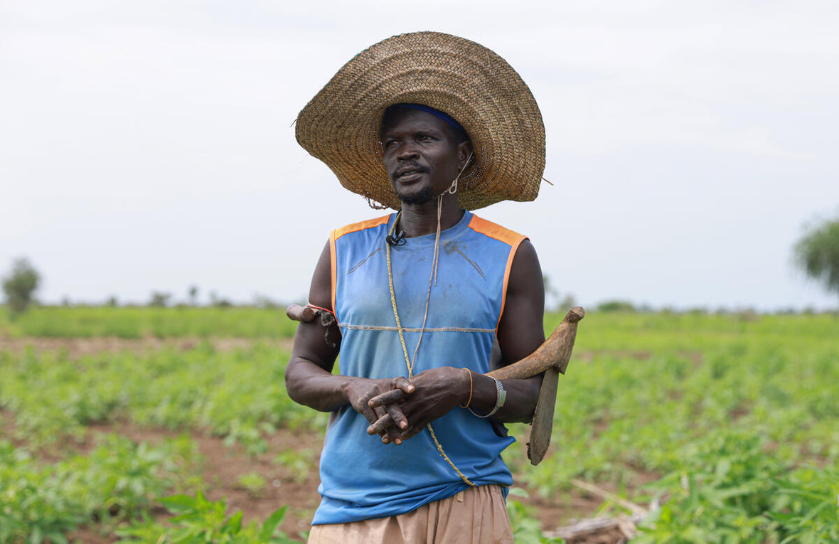  A man wearing a large, straw hat stands in a field.