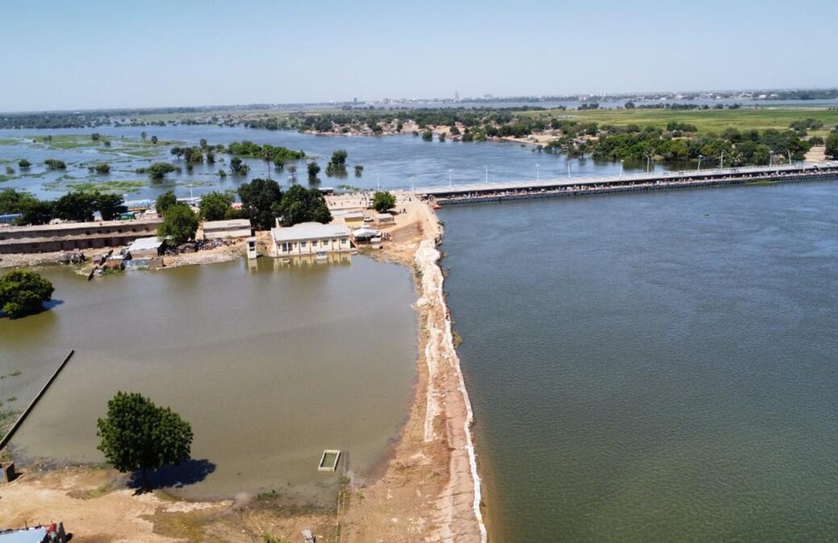Flooding surrounds buildings, trees and a long bridge.