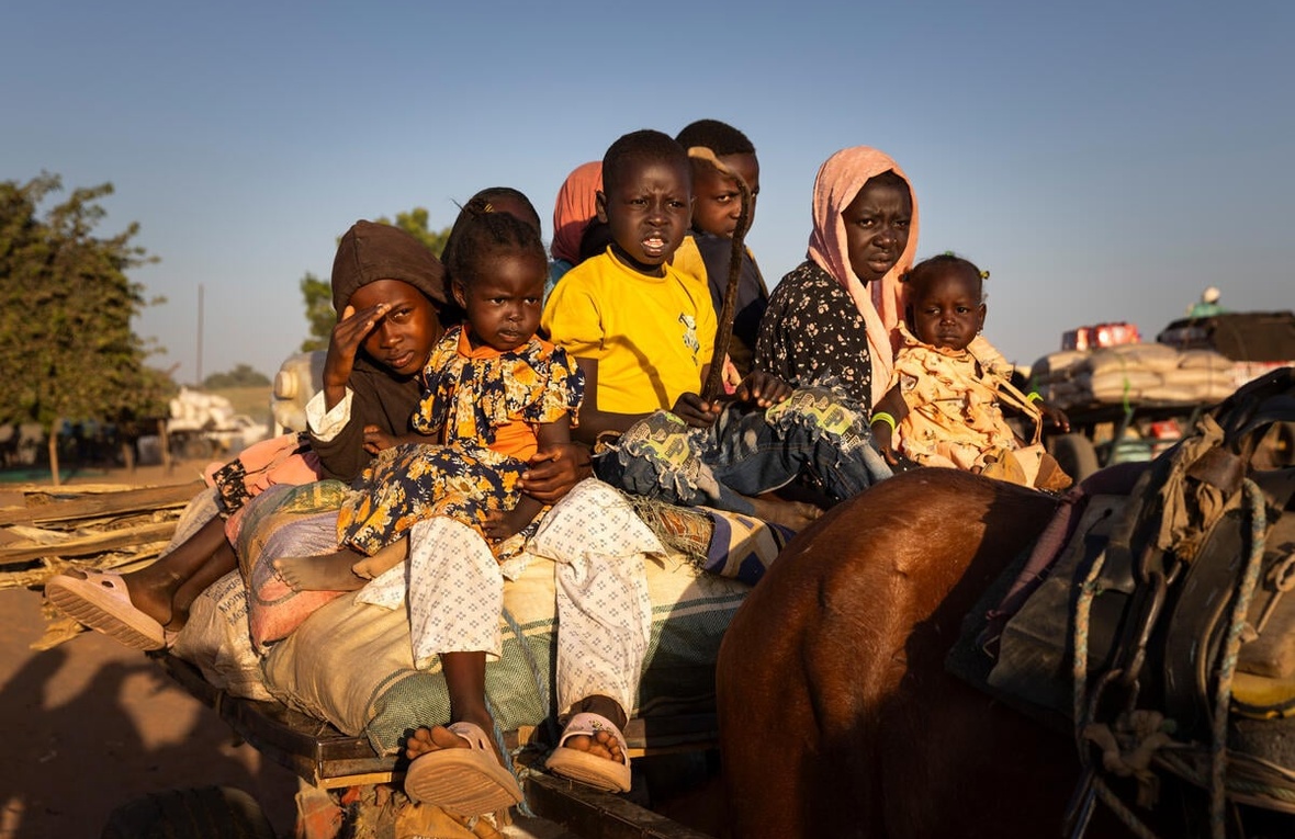 A group of Sudanese children sit on top of a cart behind a horse.
