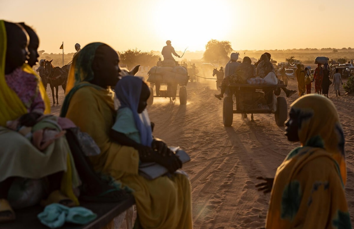 The sun lights up the dust behind groups of Sudanese refugees walking and on carts behind horses