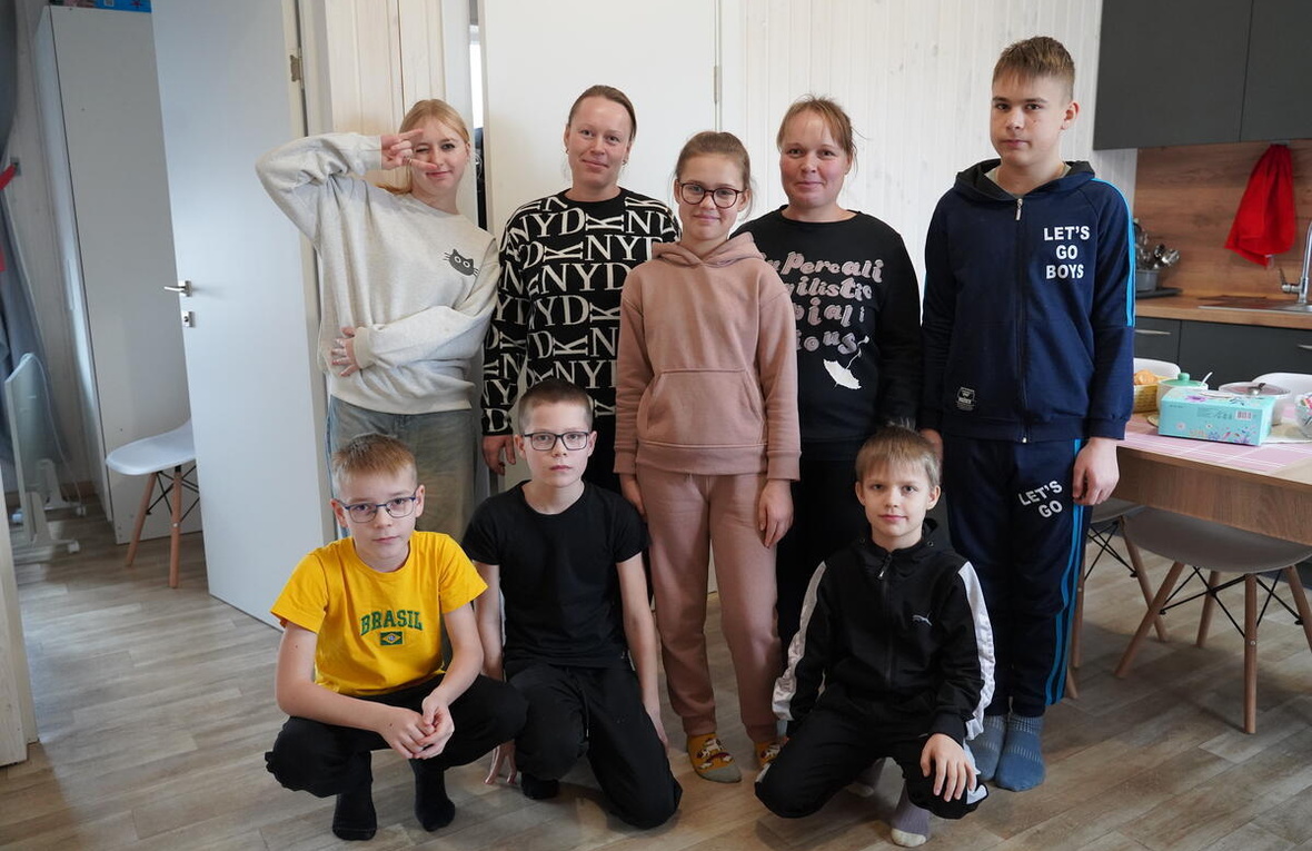 Two mothers surrounded by their six children gather for a group photo in their kitchen