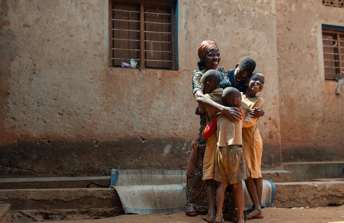 A Burundian woman hugs four of her children standing outside a building with a huge smile on her face