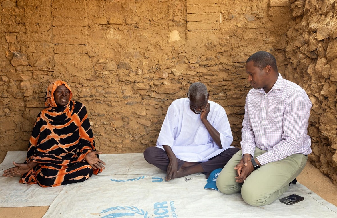 Mamadou Dian Balde sits on the floor, speaking with two Sudanese refugees.