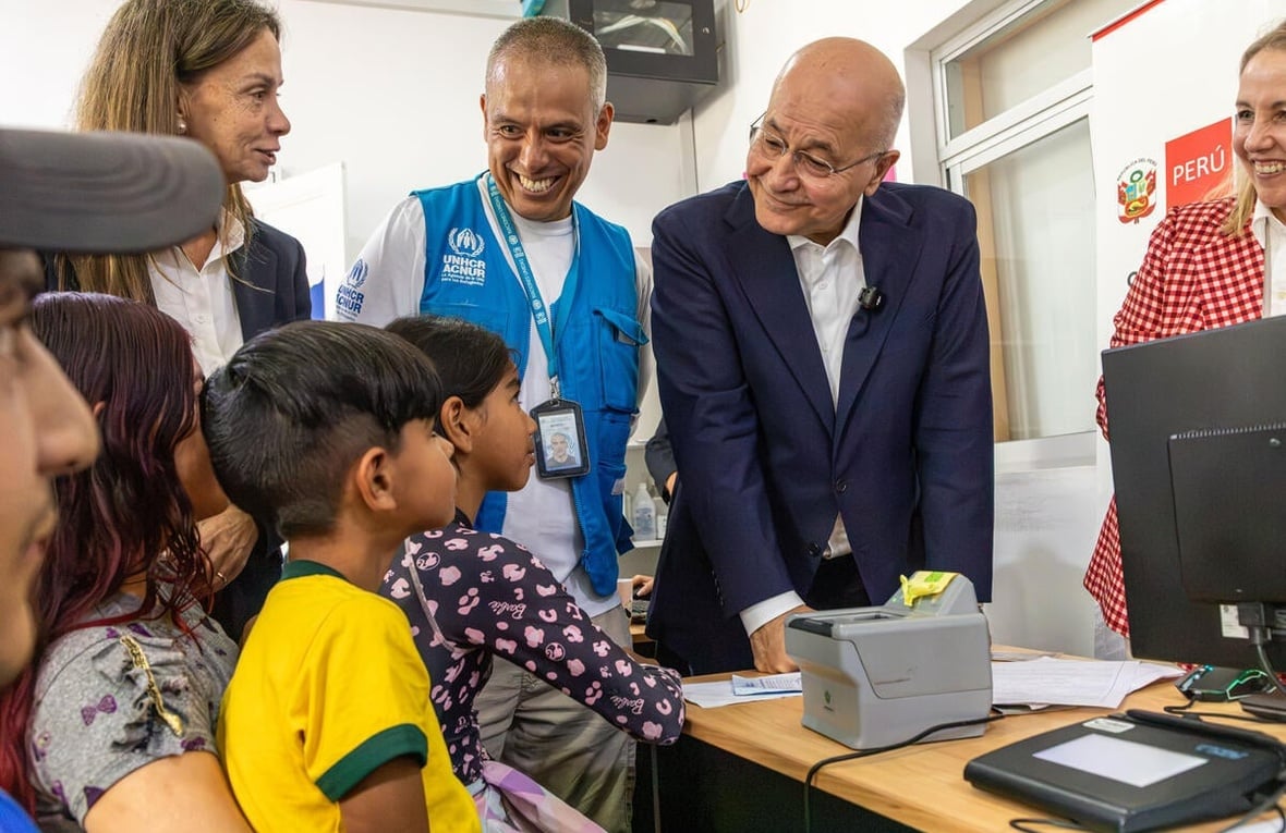 Barham Salih and UNHCR colleagues speak with a family sitting behind a desk with a computer. Everyone is smiling.