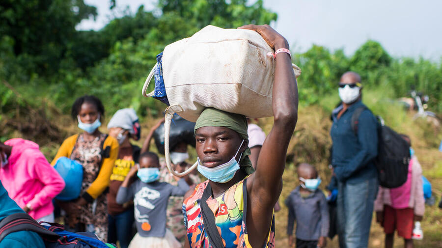 A refugee returning home to Côte d'Ivoire holds a bag on his head as he walks with other refugees.
