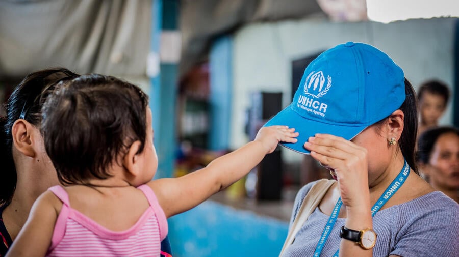 A young child grabs a woman's UNHCR blue cap