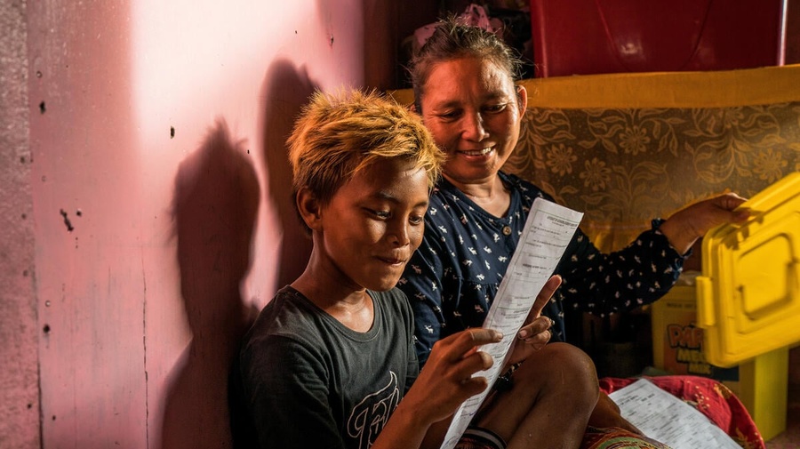 A young Filipino boy smiles as he reads his name on his birth certificate while his mother looks on. 