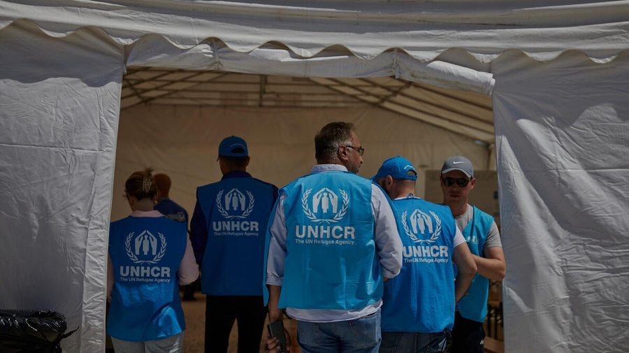 A group of UNHCR staff members walk inside a white emergency tent. 