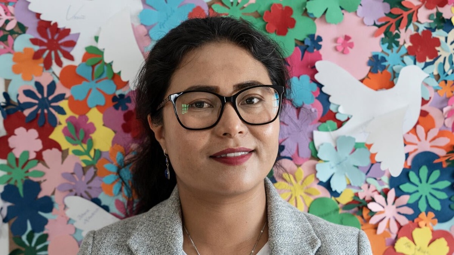A woman stands in front of a wall decorated with flowers.