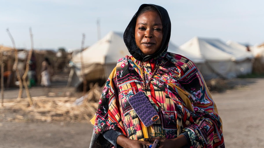 A woman in a colourful dress stands in front of rows of white tents in an IDP camp.