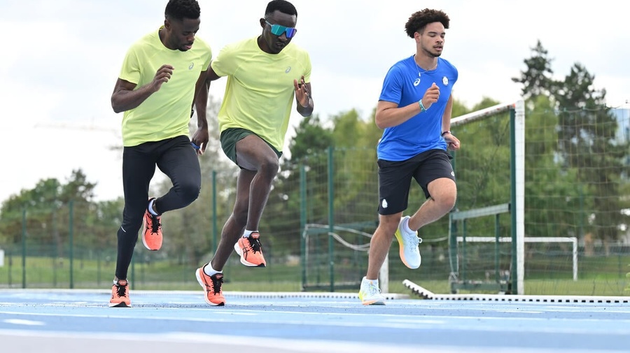 Three athletes run in parallel on a blue running track.