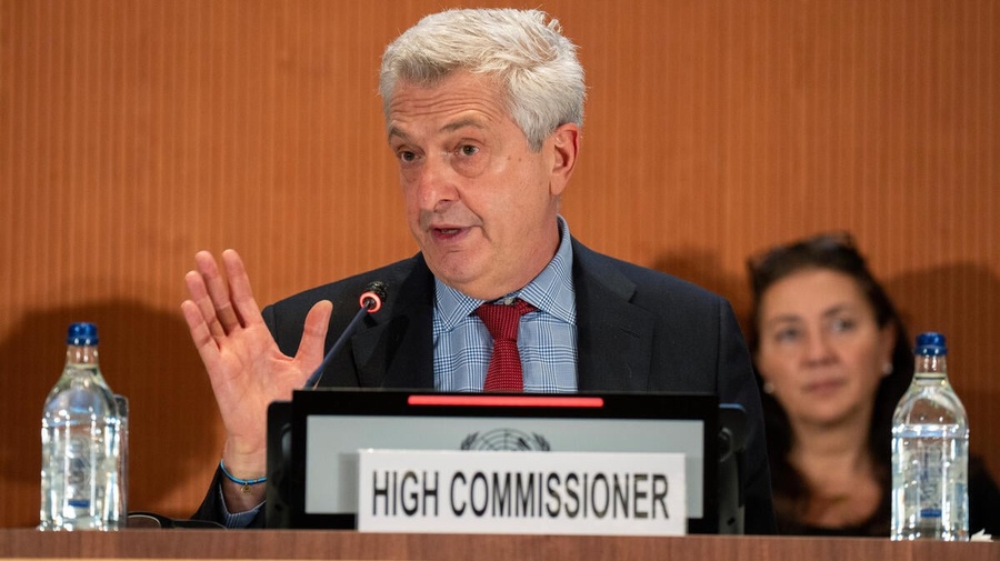 A man sits behind a dais making a speech with a sign reading 'High Commissioner' in front of him