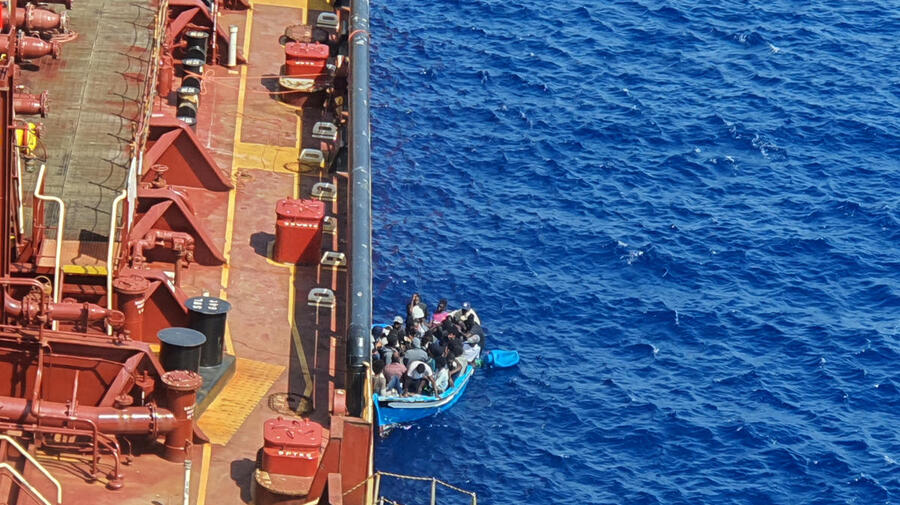 Malta. Migrants sit in a boat alongside the Maersk Etienne tanker