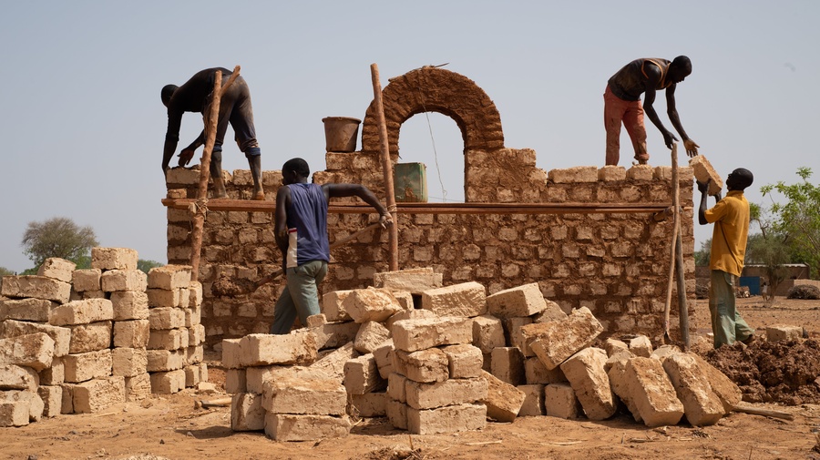 Personas desplazadas internas de Burkina Faso reciben capacitación por parte de albañiles locales para construir casas respetuosas con el clima utilizando materiales locales en Kaya, Burkina Faso.