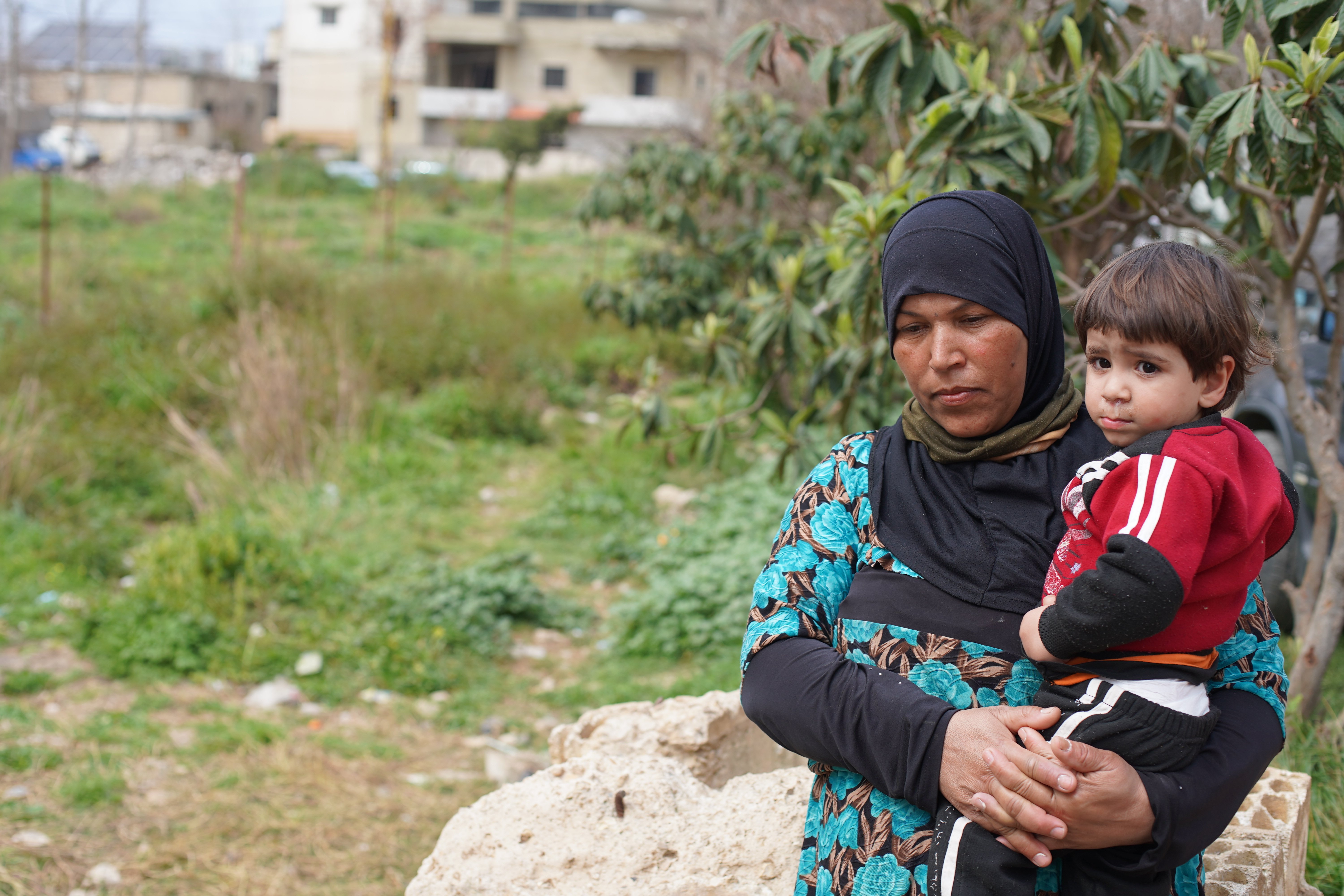 A Syrian woman holds her young nephew in a field near their home