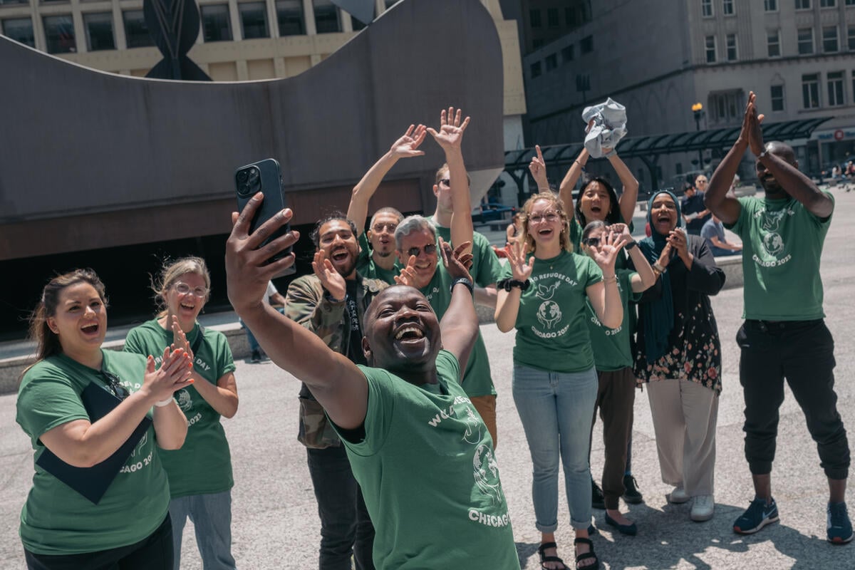 A group of smiling, cheering people take a selfie in Chicago at World Refugee Day celebrations