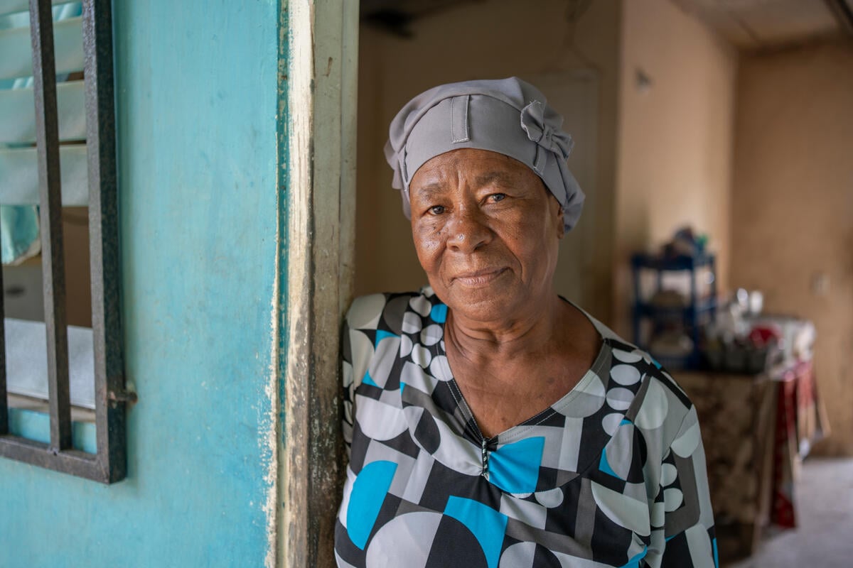 An older woman stands in the doorway of a house.