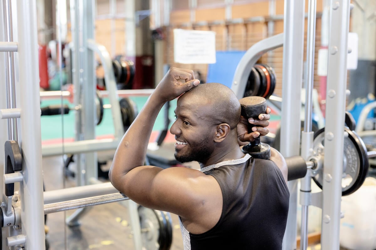 A man leans on a weight-lifting machine while holding a weight in one hand.
