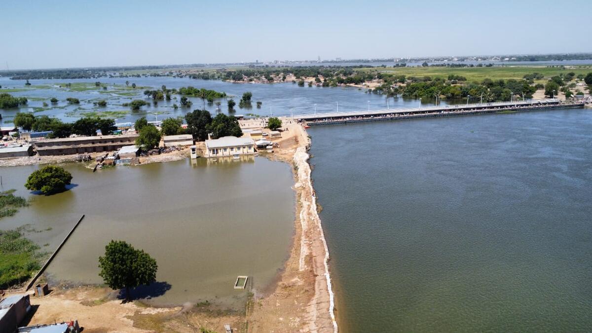Flooding surrounds buildings, trees and a long bridge.