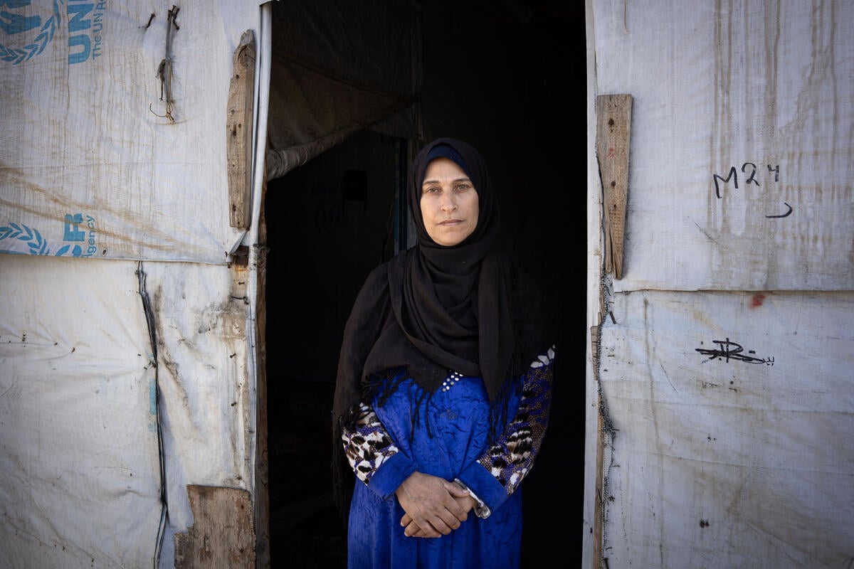 A woman wearing a headscarf stands at the entrance to a UNHCR-branded shelter.