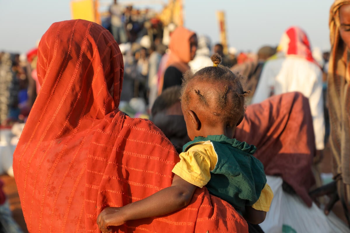 A woman in orange pictured from behind, carrying her child.
