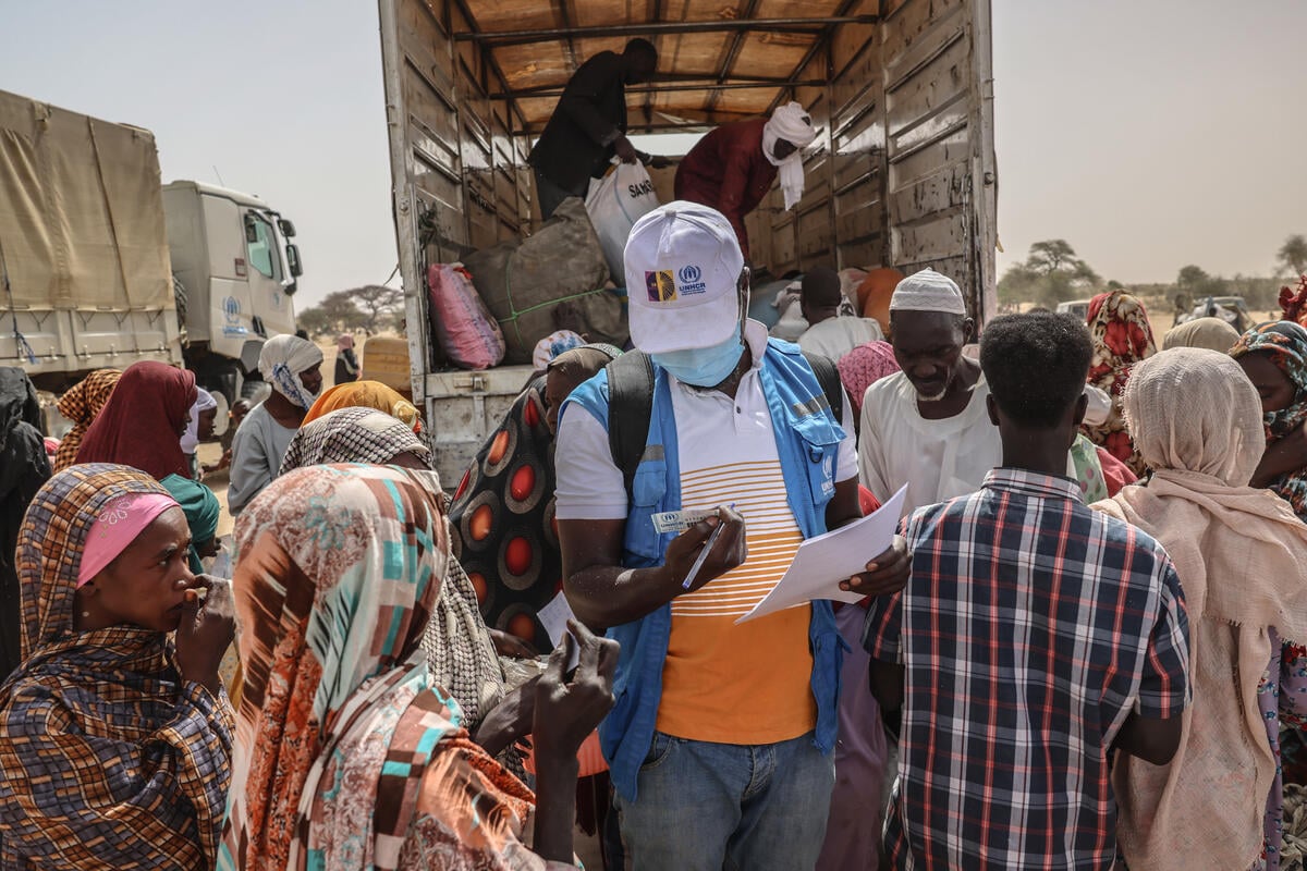 A UNHCR staff member checks documents in a group of people standing at the back of an open truck.