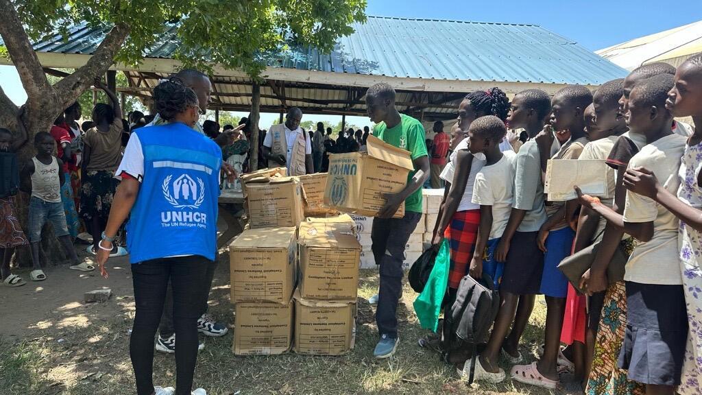 Women and children line up to receive aid packages in boxes from a UNHCR staff member.