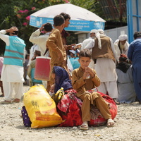 A young Afghan boy sits on piles of luggage, while others stand behind.