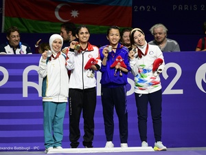 Four women stand alongside each other holding up medals around their necks.