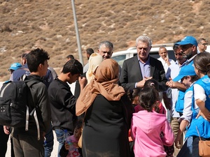 A man in a suit and others in UN clothing talk to a family outside with a vehicle in the background