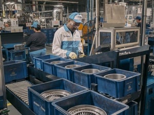 A man wearing overalls, protective eyeglasses and a cap works in an auto parts factory