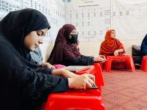 Helai Noori sits on the floor of a classroom with other women and reads Braille on a wooden tablet.