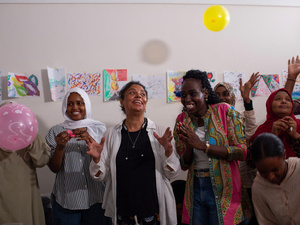 Women clap and smile and throw balloons in the air.