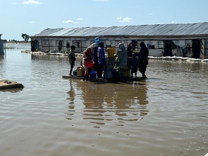 Women and children gather around a water point surrounded by floodwaters.