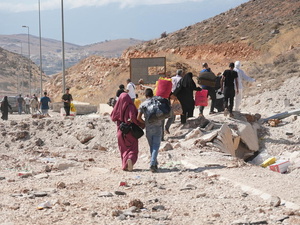 People carry their belongings down a rubble-strewn road with hills on either side