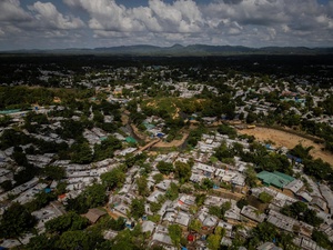 An aerial view of a huge refugee camp, trees throughout, with mountains in the background