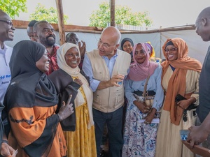 A group of men and women smile while standing and talking in an outdoor shaded structure