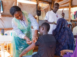 Several people receive vaccinations and other medical consultation in a makeshift shelter outdoors