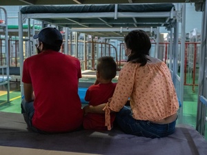 Honduran returnees sitting on a bed in the Kiki Romero gymnasium, a space enabled by the local government to provide care to people under Title 42.