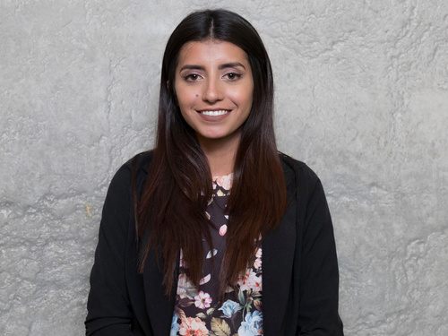 Portrait of a young woman standing against a grey background.