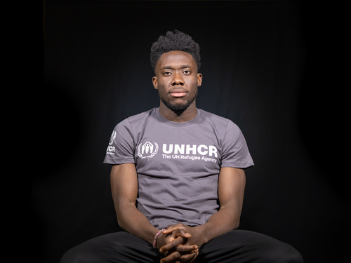 Alphonso Davies sitting in chair, wearing UNHCR t-shirt 