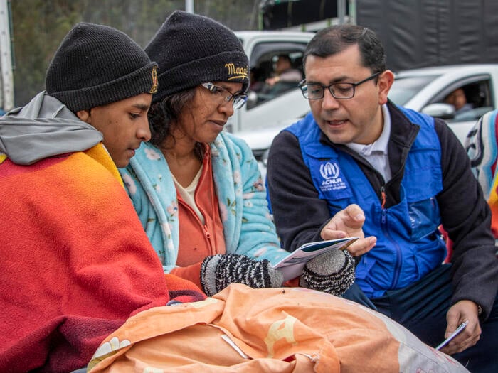 A UNHCR staff member explains a pamphlet to a man and a woman.