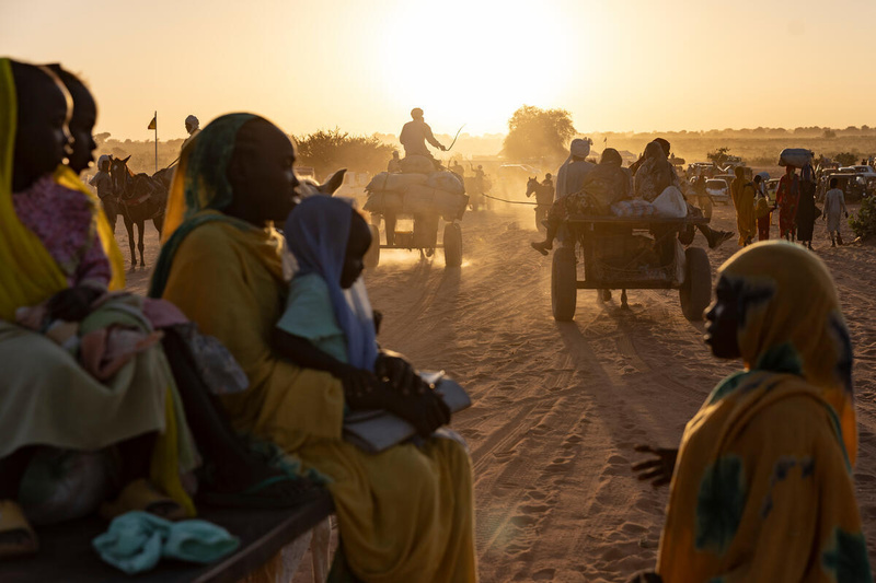 The sun lights up the dust behind groups of Sudanese refugees walking and on carts behind horses