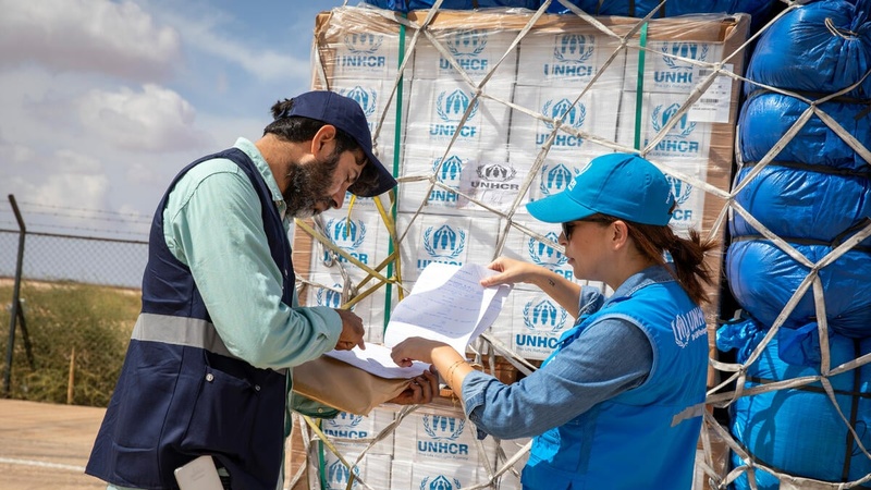 Two UNHCR staff members check a shipment of emergency supplies against a list