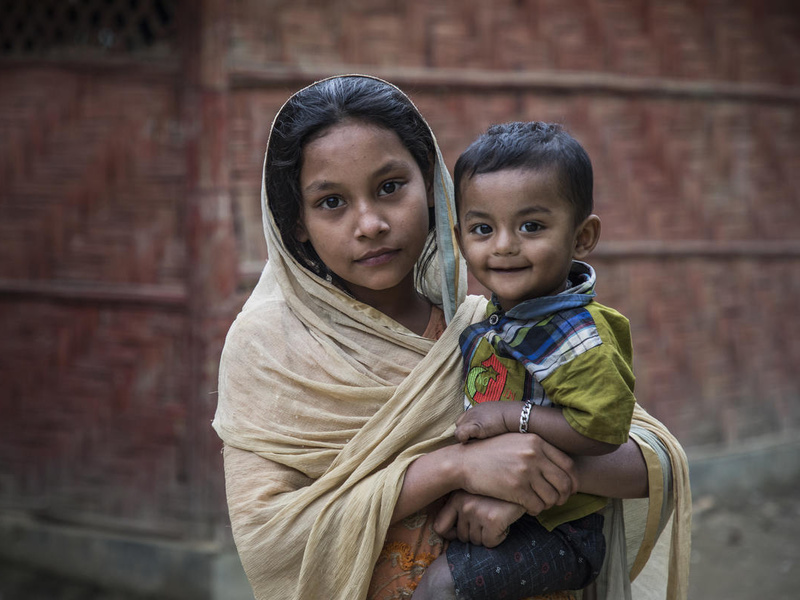 A young Rohingya girl holds her little brother